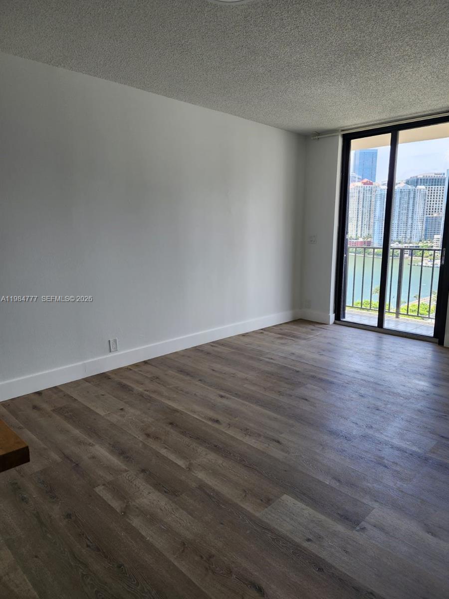 An empty room features wood-look flooring, white walls, and a sliding glass door to a balcony — 520 Brickell Key Dr # A1517, Miami FL 33131, MIAMI, FL