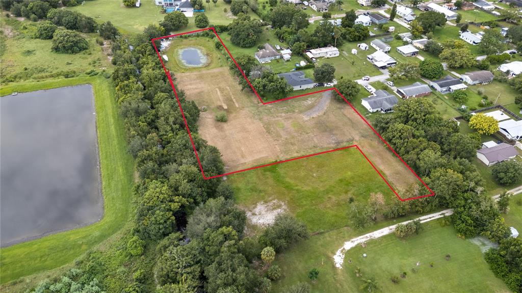 An aerial view shows a vacant, L-shaped residential lot outlined in red with a pond — 1819 KENTUCKY AVENUE, ST CLOUD, FL