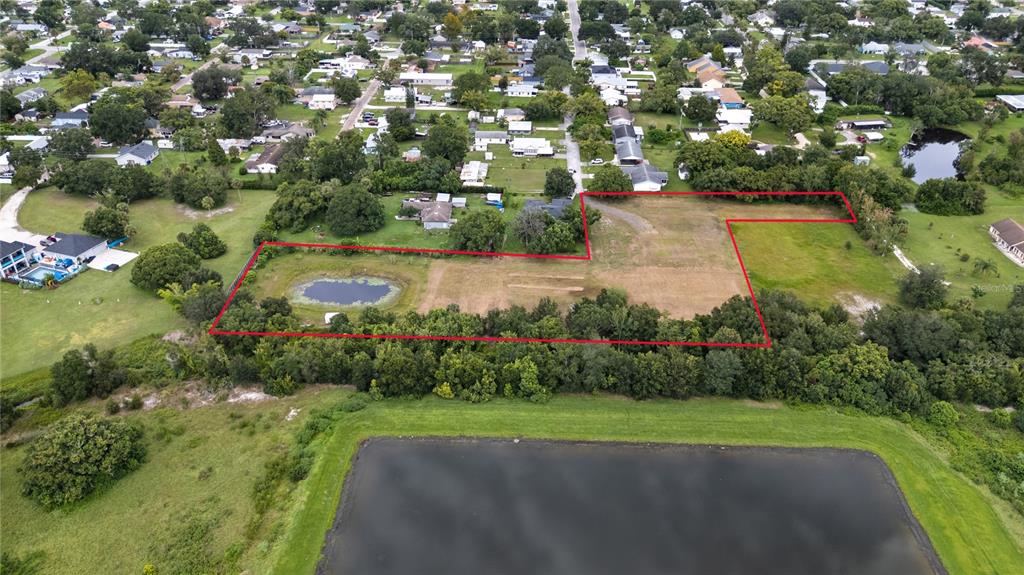 An aerial view shows a large, vacant rectangular lot outlined in red with a pond — 1819 KENTUCKY AVENUE, ST CLOUD, FL