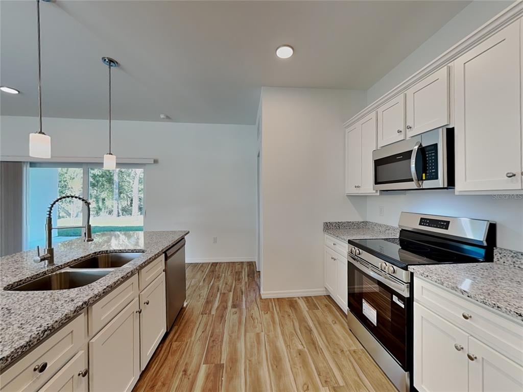 A kitchen features white cabinets, granite countertops, stainless steel appliances, and wood-look flooring — 5281 GILLOT BOULEVARD, PORT CHARLOTTE, FL