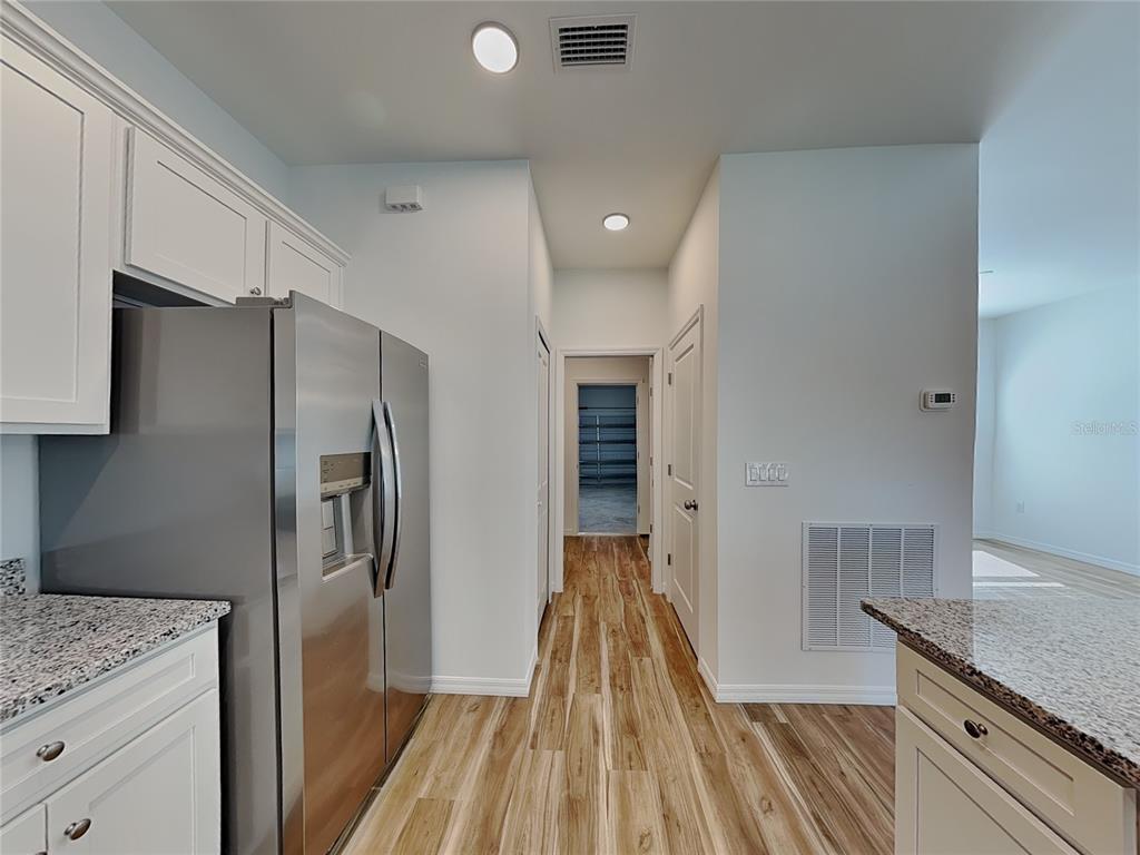 A kitchen hallway features white cabinets, stainless steel appliances, granite countertops, and wood-look flooring — 5281 GILLOT BOULEVARD, PORT CHARLOTTE, FL