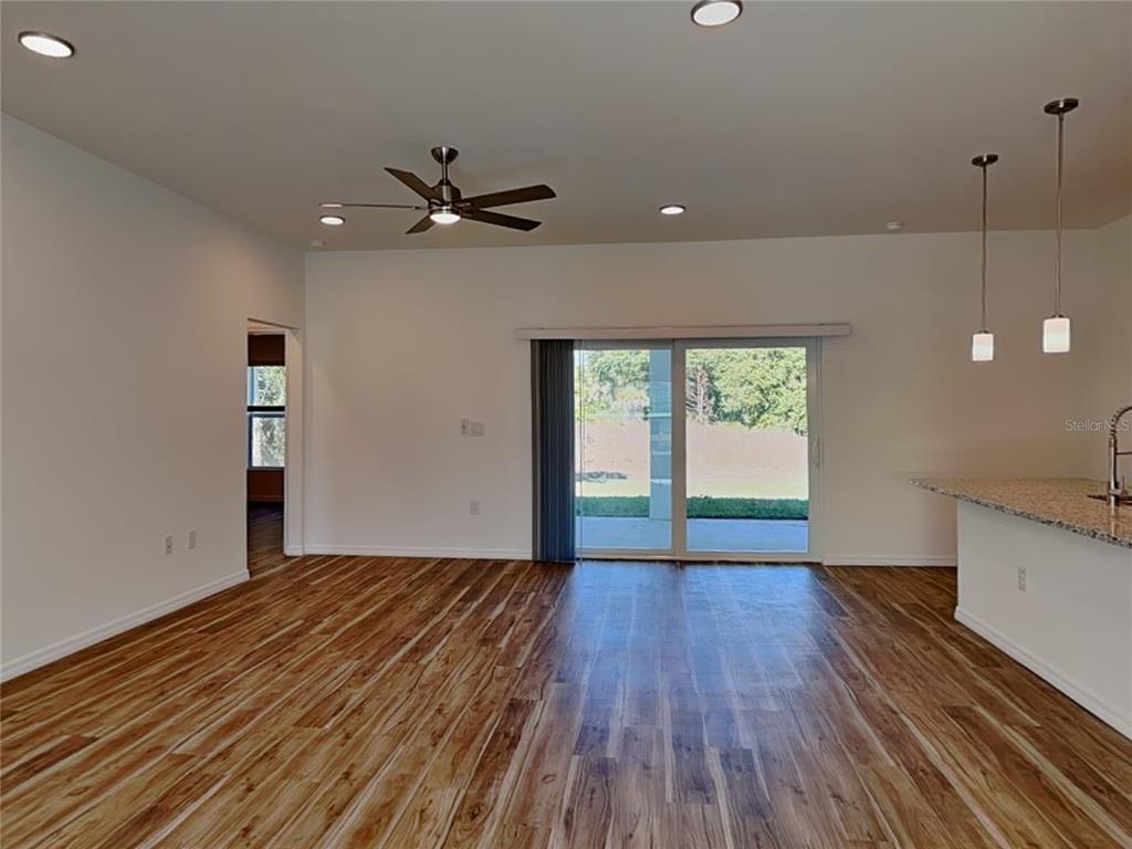 An open-concept living area features wood-look flooring, a ceiling fan, and sliding glass patio doors — 5281 GILLOT BOULEVARD, PORT CHARLOTTE, FL