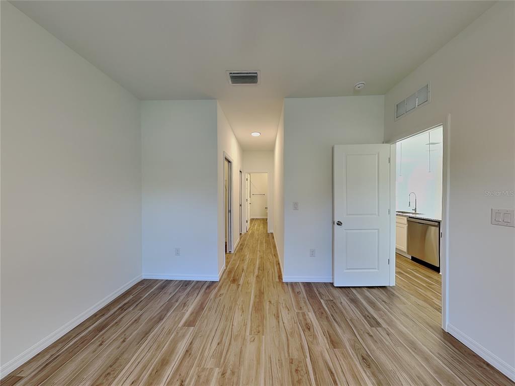 A hallway with wood-look flooring leads to a room with an open doorway to a kitchen — 5281 GILLOT BOULEVARD, PORT CHARLOTTE, FL