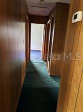 A narrow hallway features wood-paneled walls, a green carpeted floor, and a white thermostat — 2114 SW 7TH STREET, OCALA, FL