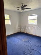 An empty bedroom features blue carpeting, white walls, two windows, and a ceiling fan — 2114 SW 7TH STREET, OCALA, FL