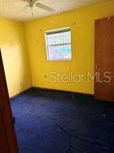 An empty bedroom features yellow walls, blue carpeting, a ceiling fan, and a wooden door — 2114 SW 7TH STREET, OCALA, FL