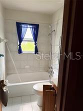 A bathroom features a white bathtub with a shower head and a blue window curtain — 2114 SW 7TH STREET, OCALA, FL