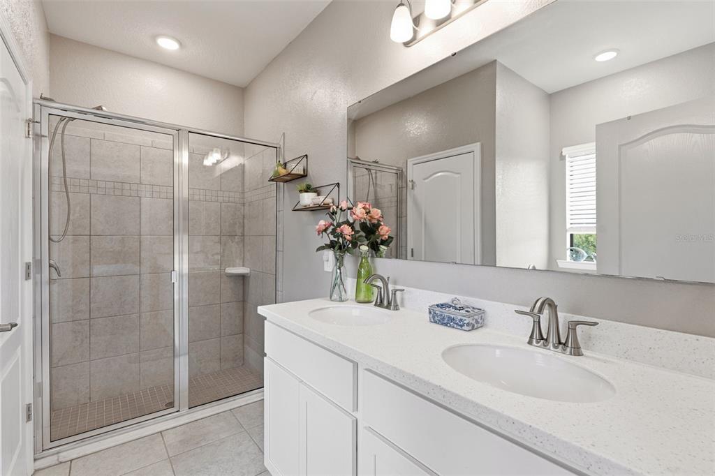 A bathroom features a double vanity with white cabinets, quartz countertops, and a glass shower — 15240 MILLE FIORE BOULEVARD, PORT CHARLOTTE, FL