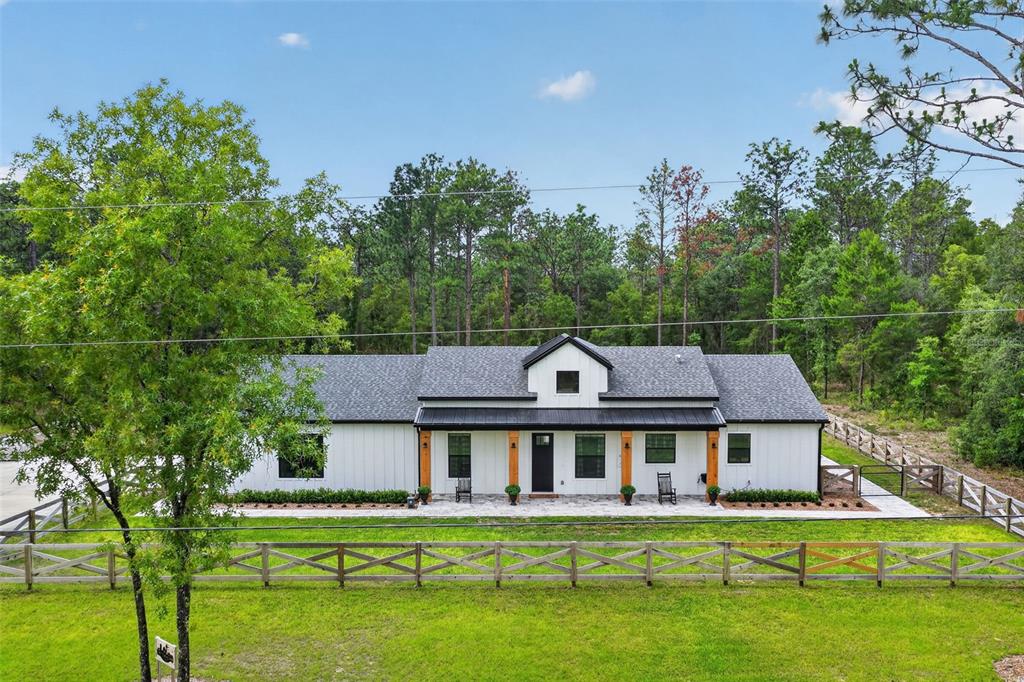 A white farmhouse with a black metal roof and wooden porch posts behind a fence — 12552 SW 78TH PLACE, DUNNELLON, FL