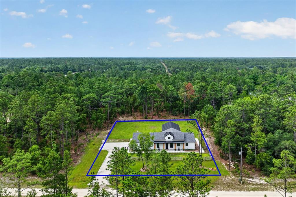 An aerial view shows a modern house with a dark roof situated on a wooded lot — 12552 SW 78TH PLACE, DUNNELLON, FL