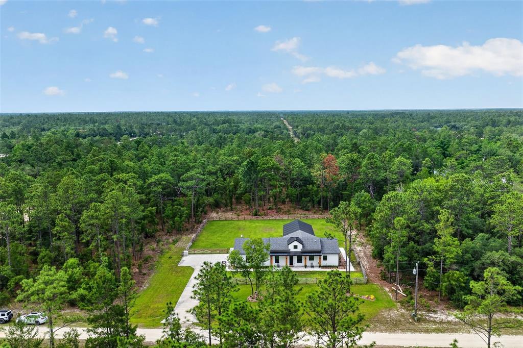 An aerial view shows a modern house with a dark roof surrounded by dense forest — 12552 SW 78TH PLACE, DUNNELLON, FL
