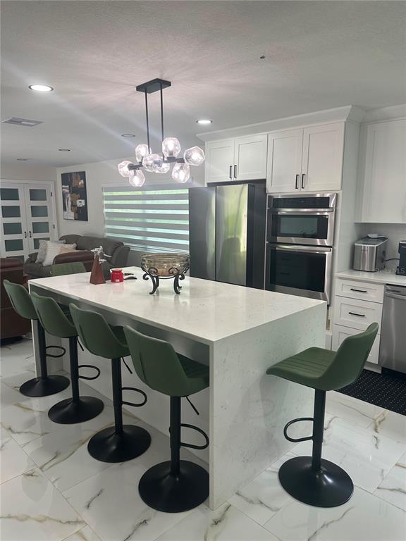 A modern kitchen features a white quartz island with four green stools and stainless appliances — 7251 NE 227TH PLACE, CITRA, FL
