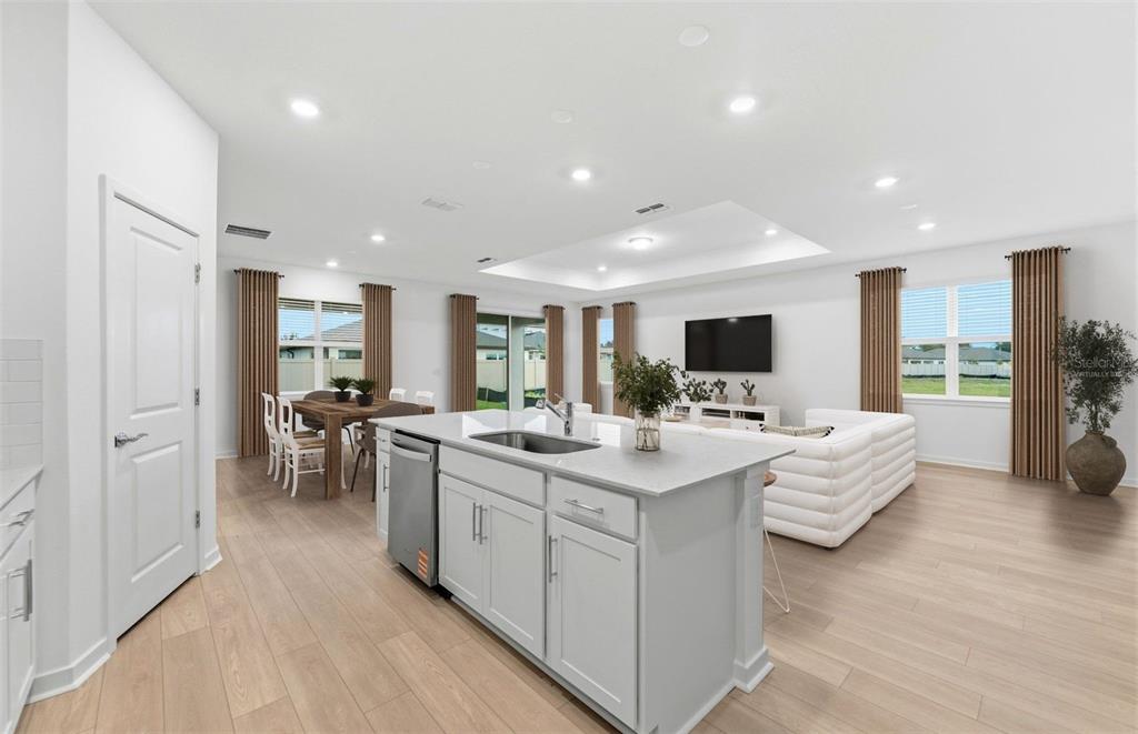 A kitchen island with a stainless steel dishwasher overlooks an open-concept living and dining area — 6607 ASBURY BARNES LANE, WESLEY CHAPEL, FL