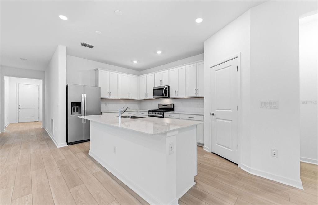 A modern kitchen features white cabinets, stainless steel appliances, and a central island with countertops — 6607 ASBURY BARNES LANE, WESLEY CHAPEL, FL