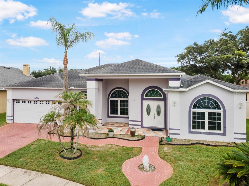 A single-story house with a white stucco facade, purple trim, a tiled walkway, and palm trees — 2087 WESTBOURNE DRIVE, OVIEDO, FL