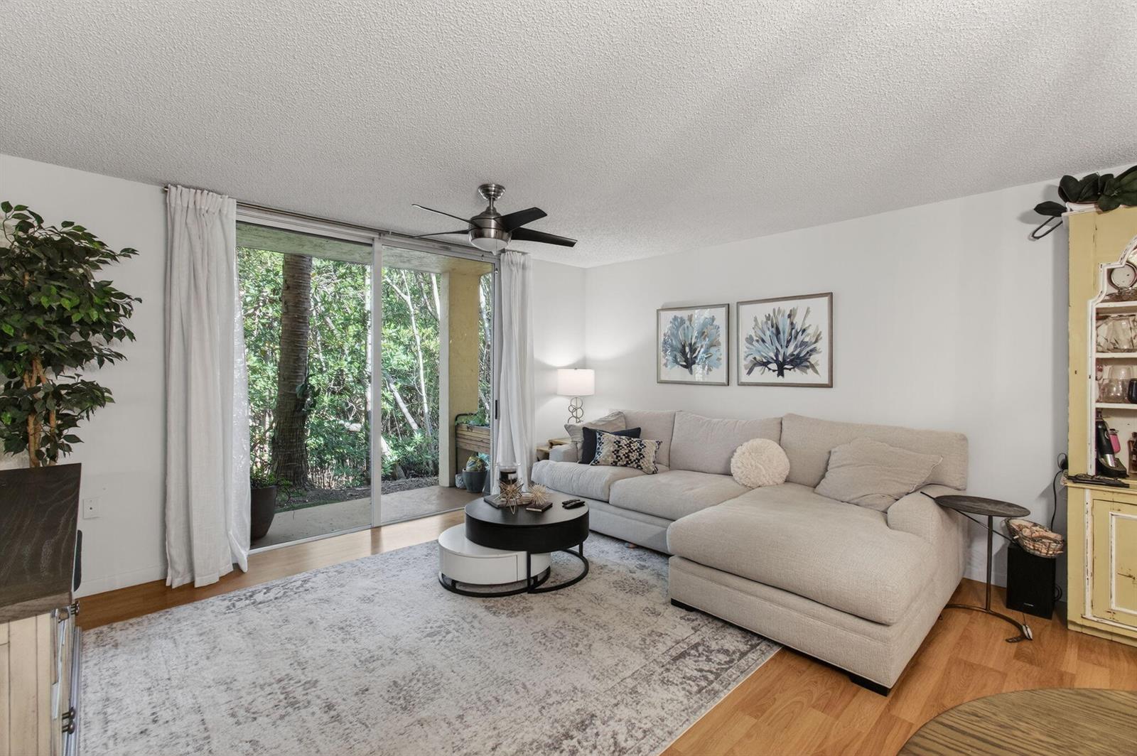 A living room with a sectional sofa, coffee table, and sliding glass doors to trees — 1100 Scotia Drive # 104, Hypoluxo FL 33462, HYPOLUXO, FL