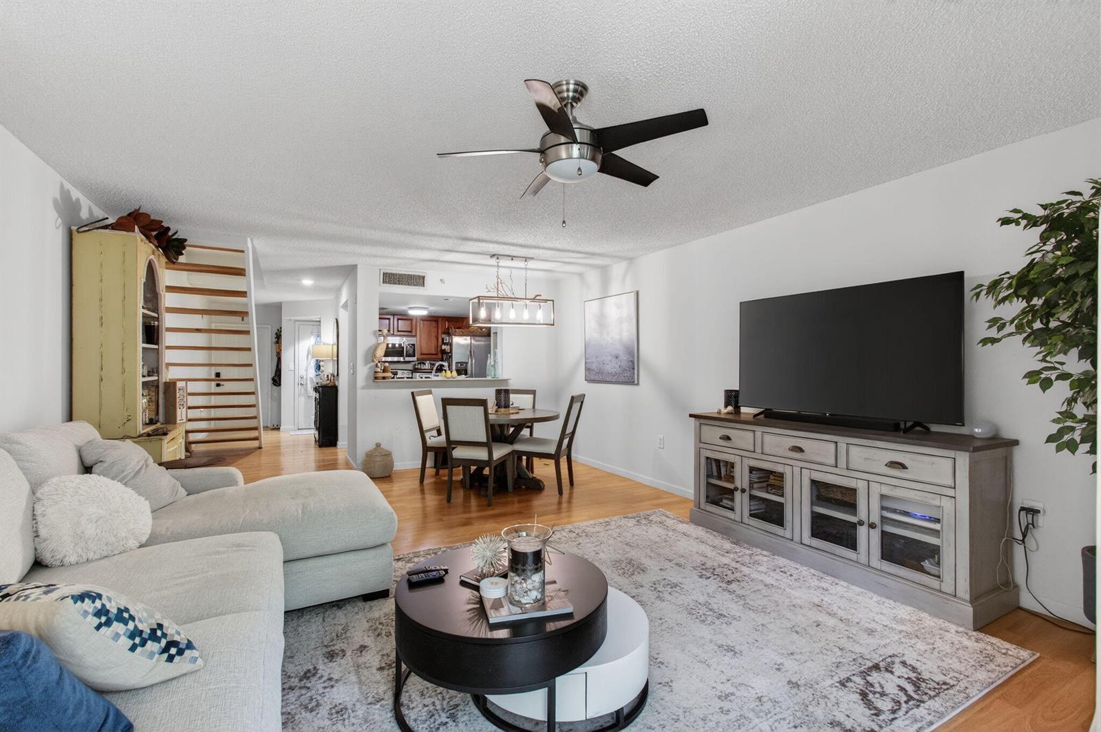 A living room with a sectional sofa, television console, dining area, and wooden staircase — 1100 Scotia Drive # 104, Hypoluxo FL 33462, HYPOLUXO, FL