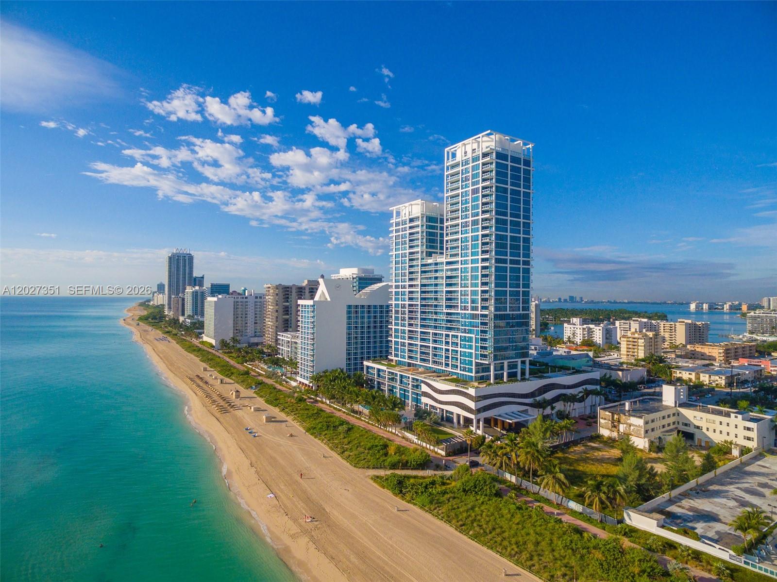 An aerial view of a tall glass condominium tower situated along a sandy beach — 6801 Collins Ave # 806, Miami Beach FL 33141, MIAMI BEACH, FL