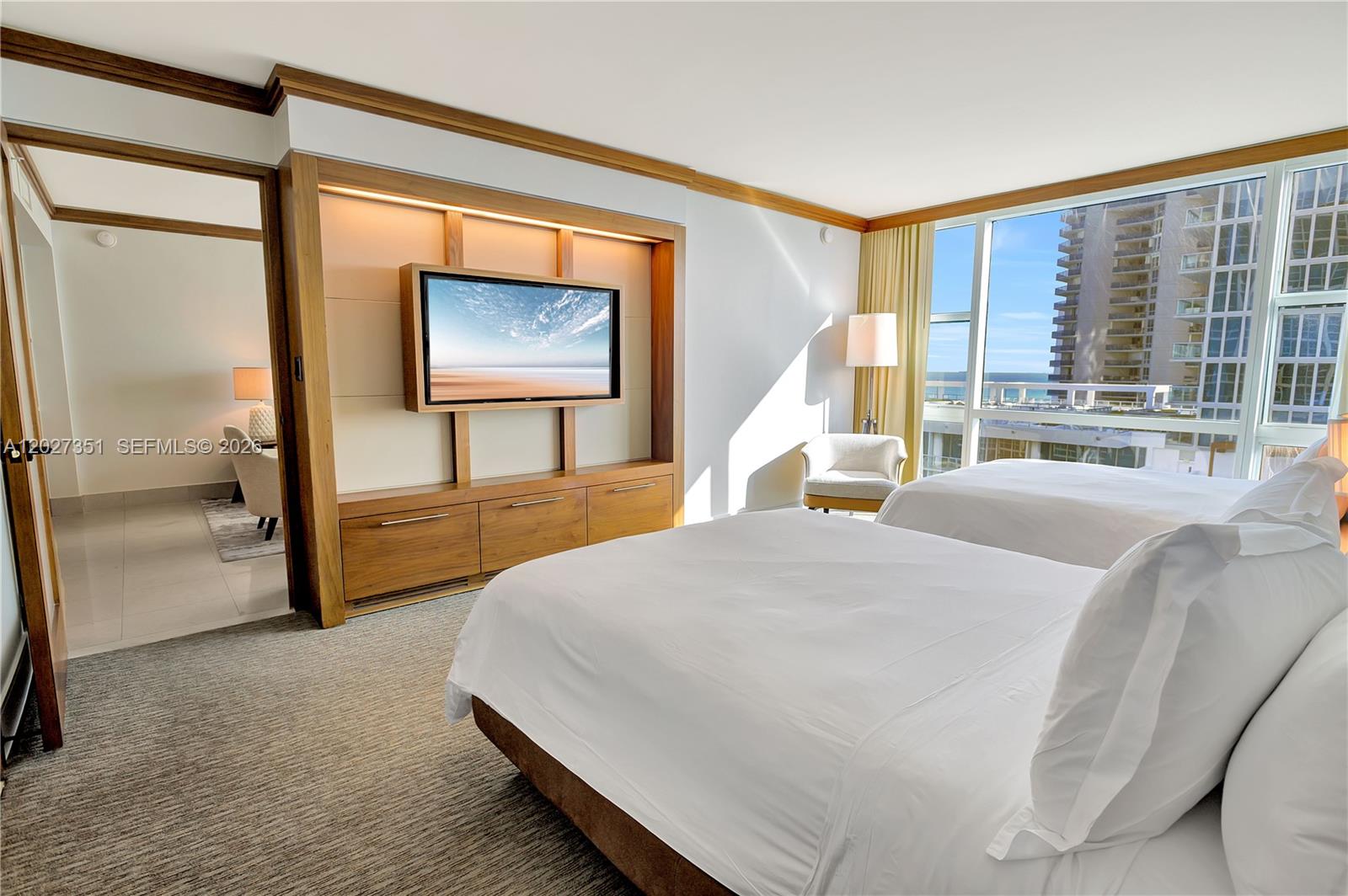 A hotel-style bedroom features two beds, a wooden media console, and floor-to-ceiling ocean views — 6801 Collins Ave # 806, Miami Beach FL 33141, MIAMI BEACH, FL