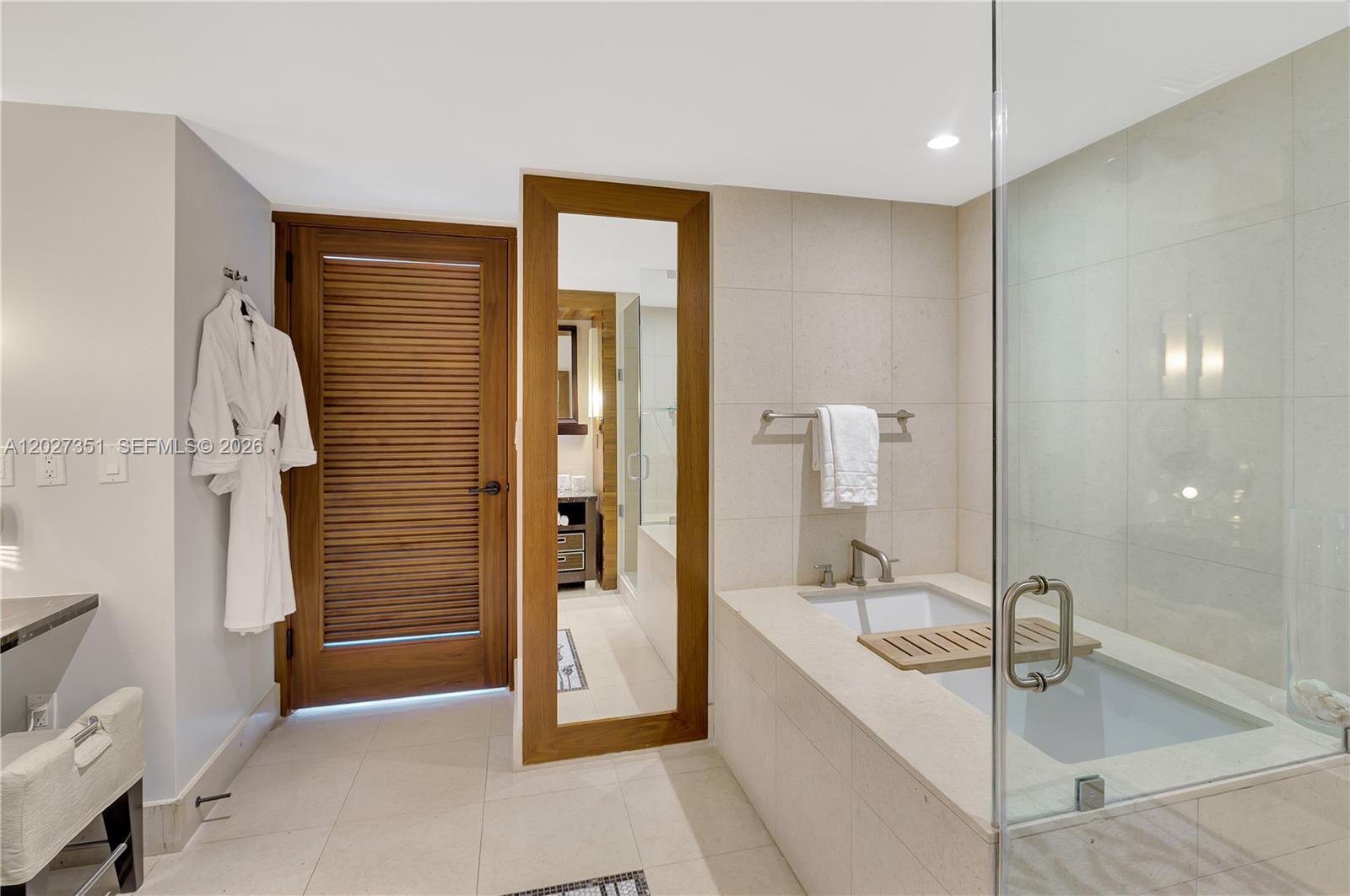 A modern bathroom features a soaking tub, a louvered wooden door, and a full-length mirror — 6801 Collins Ave # 806, Miami Beach FL 33141, MIAMI BEACH, FL