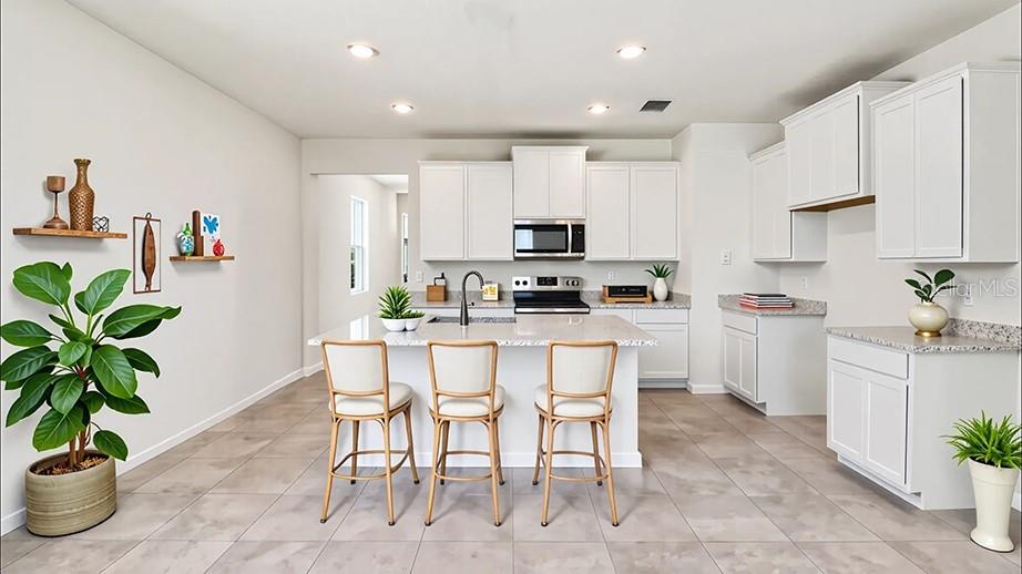 A bright kitchen features white cabinetry, a central island with three stools, and tile flooring — 4015 NW 44TH CIRCLE, OCALA, FL