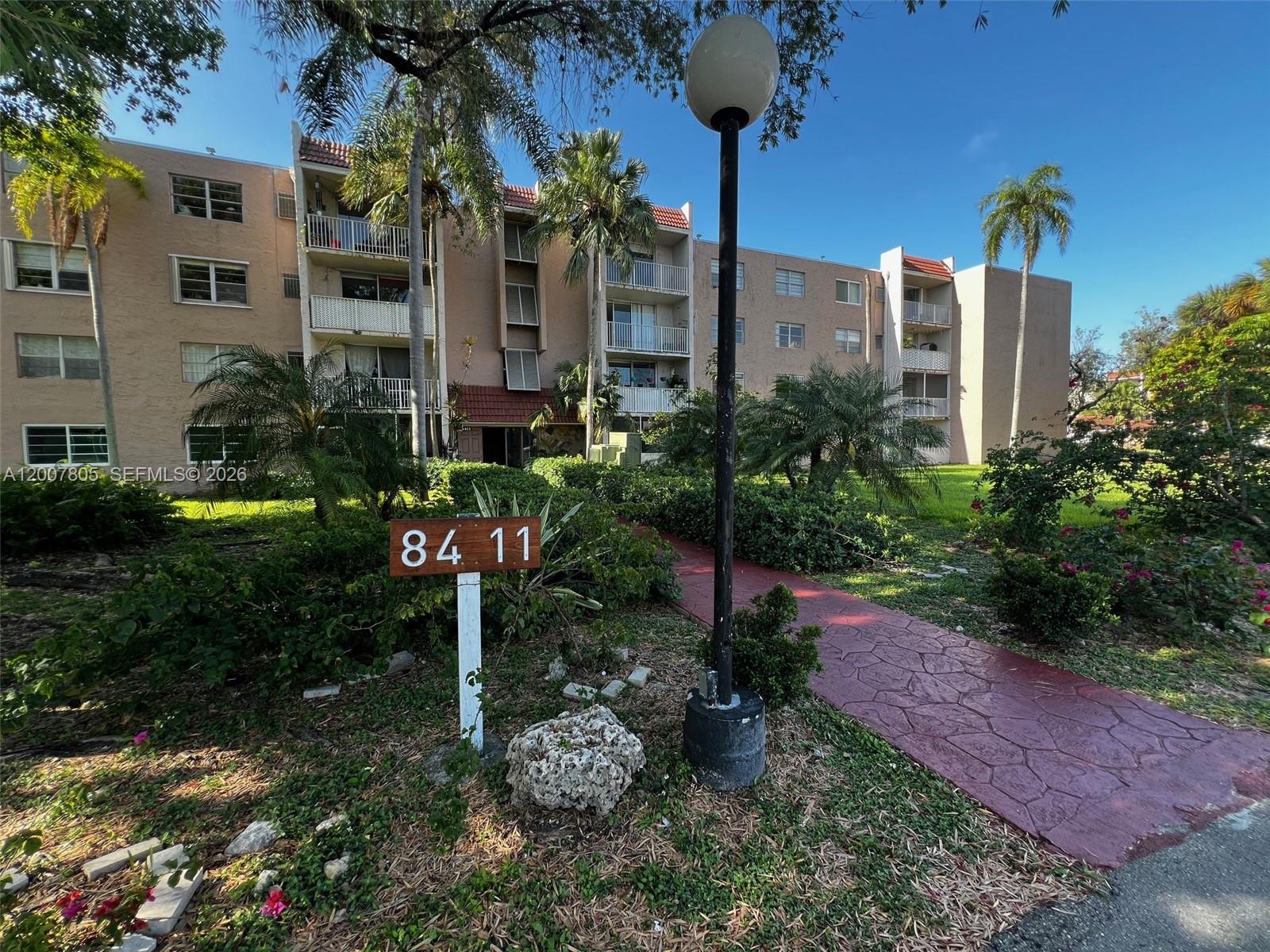 A multi-story apartment building features balconies, palm trees, and a walkway with a lamp post — 8411 NW 8th St # 105, Miami FL 33126, MIAMI, FL