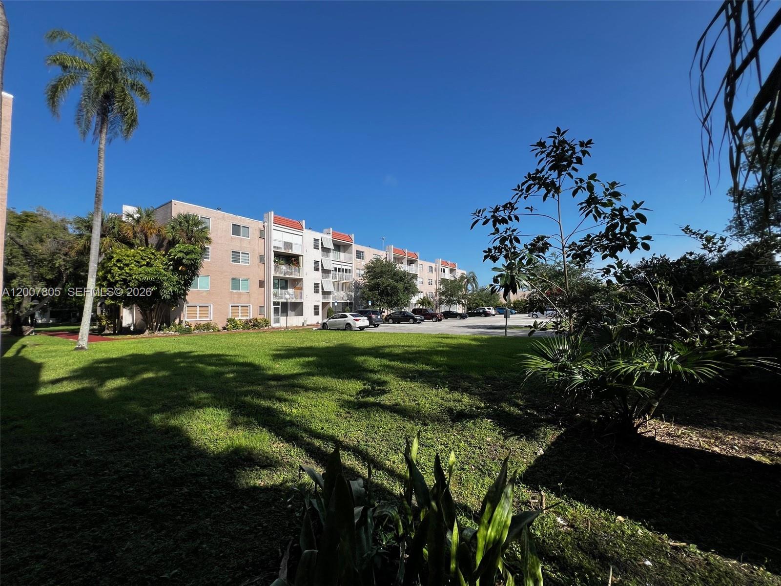 A multi-story apartment building stands behind a large grassy lawn and parking area — 8411 NW 8th St # 105, Miami FL 33126, MIAMI, FL