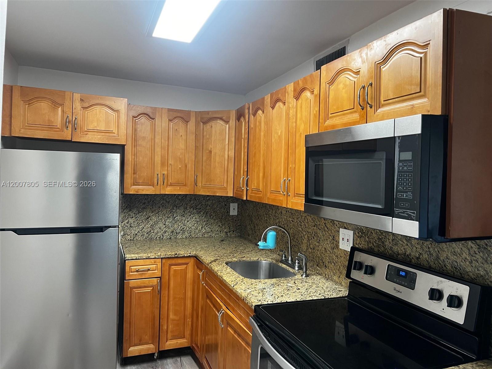 A kitchen features wooden cabinets, granite countertops, stainless steel appliances, and a double-basin sink — 8411 NW 8th St # 105, Miami FL 33126, MIAMI, FL