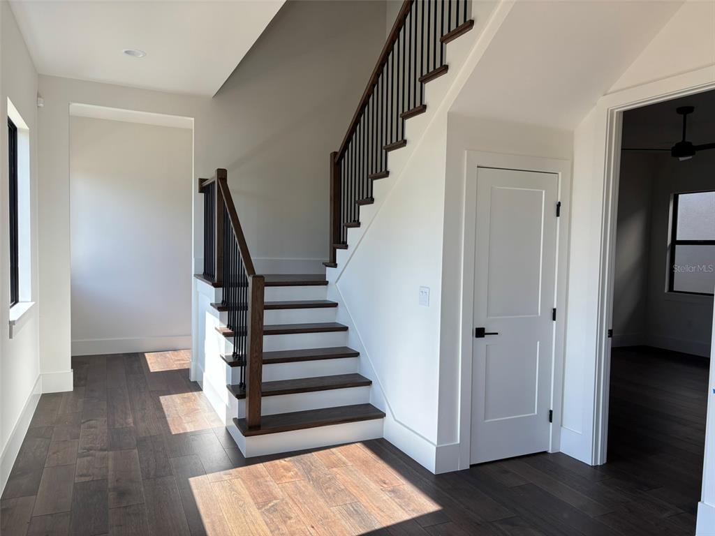 A staircase with dark wood treads and black railings stands in a room with hardwood floors — 16251 VETTA DRIVE, BELLA COLLINA, FL