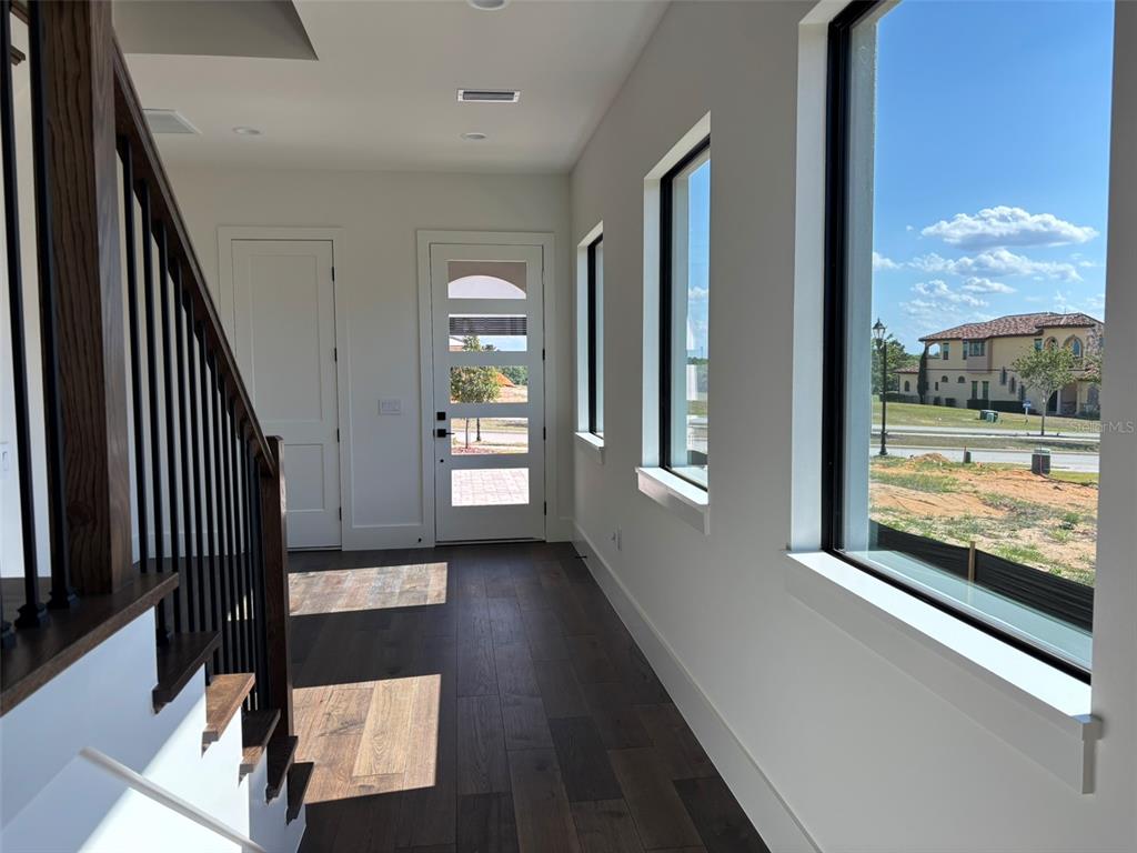 An entryway features dark wood floors, a staircase with black railings, and large windows — 16251 VETTA DRIVE, BELLA COLLINA, FL