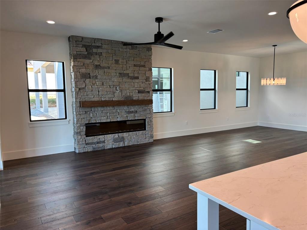 A living room features a stone fireplace, dark wood flooring, and large windows — 16251 VETTA DRIVE, BELLA COLLINA, FL