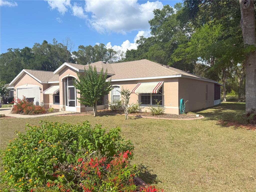 A single-story tan house with a shingled roof and red-striped awnings sits on a lawn — 1001 NE 22ND AVENUE, OCALA, FL