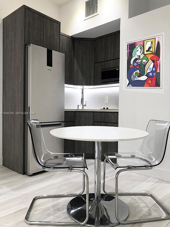 A modern kitchen area features dark wood cabinetry, a stainless steel refrigerator, and light flooring — 1915 Brickell Ave, Miami FL 33129, MIAMI, FL