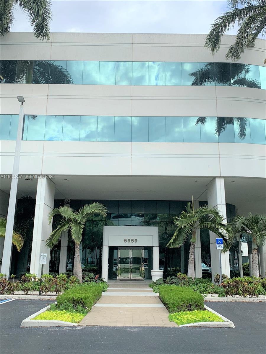 A low-angle view of a multi-story office building entrance with palm trees and landscaping — 5959 Waterford District Dr # 305, Miami FL 33126, MIAMI, FL