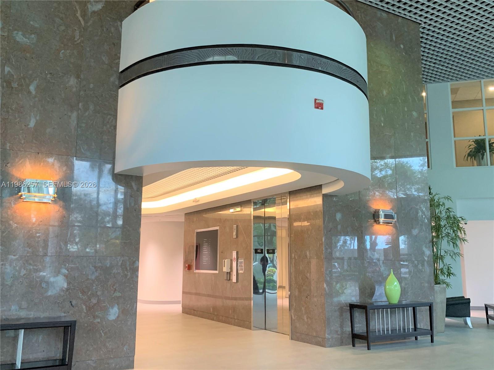 A modern lobby features marble walls, a curved white ceiling structure, and an elevator bank — 5959 Waterford District Dr # 305, Miami FL 33126, MIAMI, FL