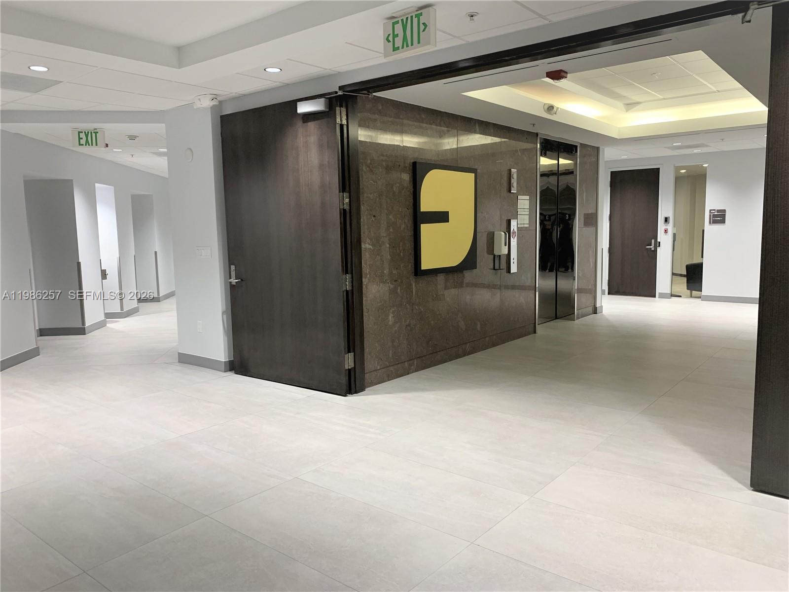 A modern office building lobby features a stone-accented elevator bank and light tile flooring — 5959 Waterford District Dr # 305, Miami FL 33126, MIAMI, FL