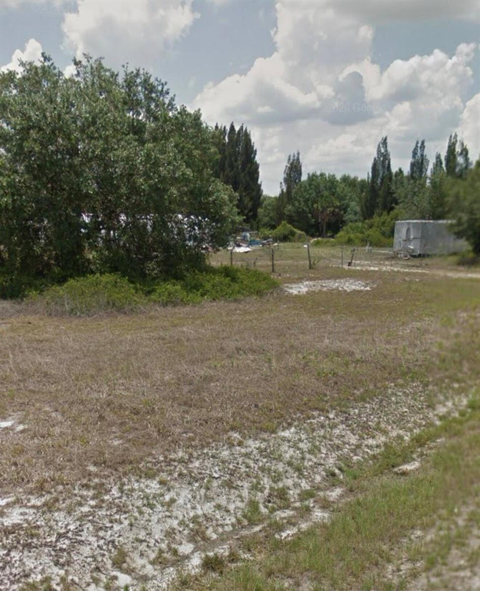 A grassy, sandy lot features a large tree, a wire fence, and a storage trailer — 160 N Coral Street, Clewiston FL 33440, CLEWISTON, FL