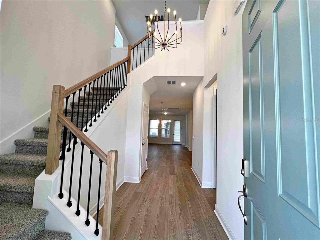 A bright entryway features a staircase with black railings, wood flooring, and a modern chandelier — 11965 BRACCO STREET, WINTER GARDEN, FL