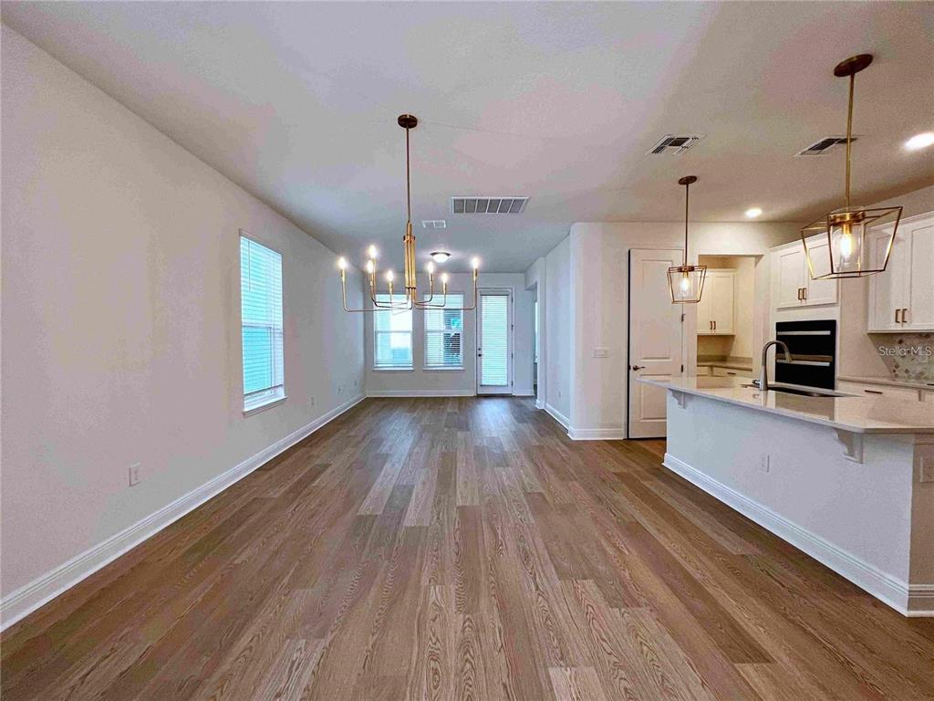 An open-concept kitchen and dining area features light wood flooring, white cabinetry, and pendant lighting — 11965 BRACCO STREET, WINTER GARDEN, FL