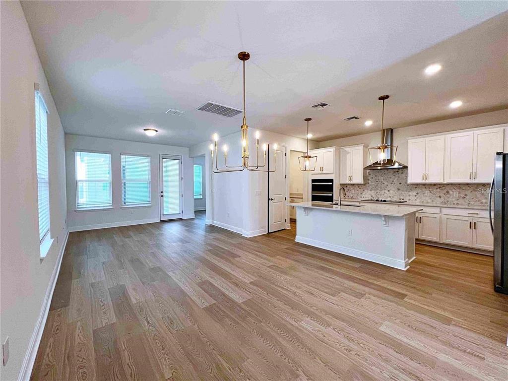 An open-concept kitchen and dining area features light wood flooring, white cabinetry, and pendant lighting — 11965 BRACCO STREET, WINTER GARDEN, FL