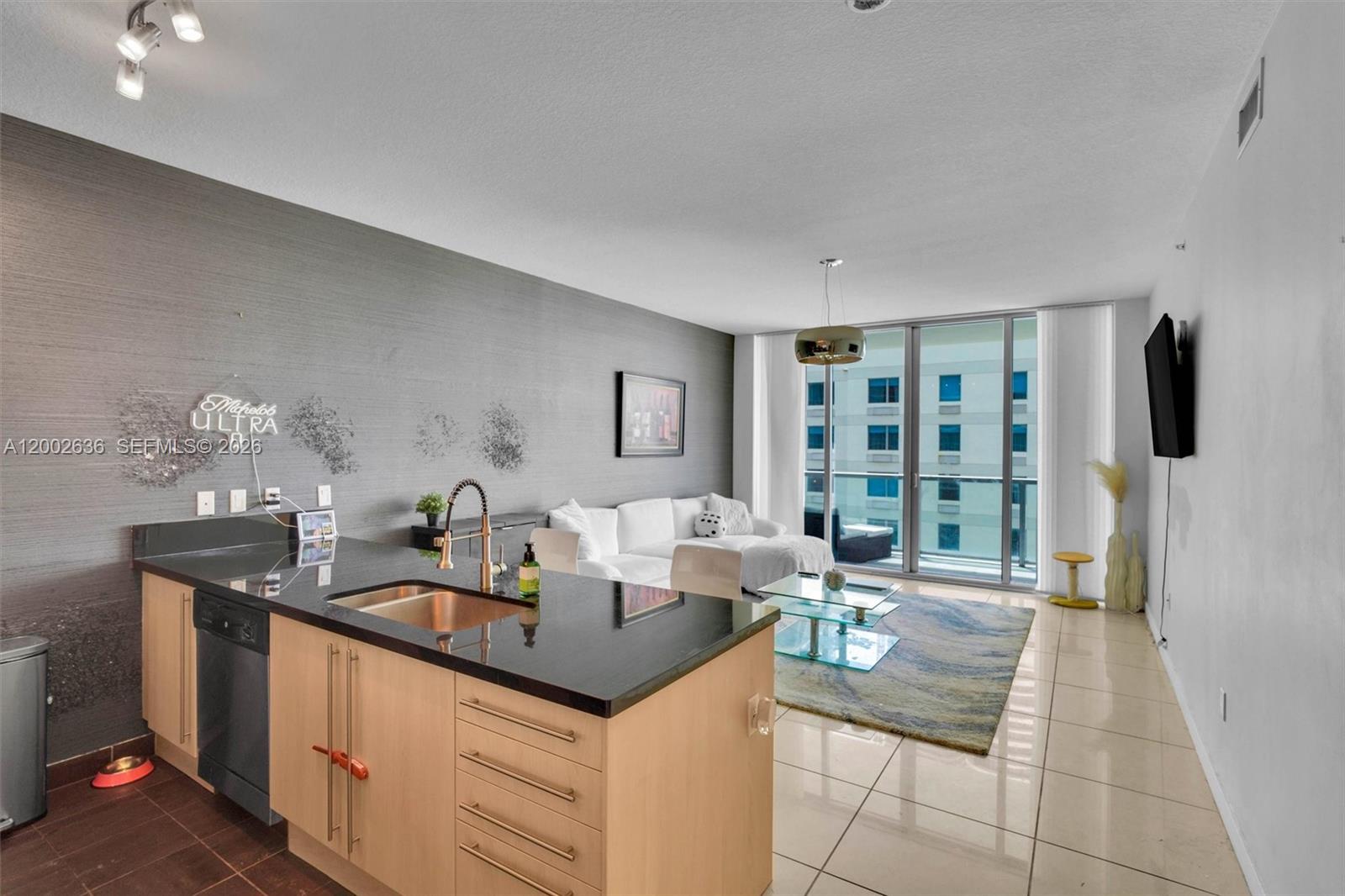 A modern open-concept living area features a kitchen island, gray accent wall, and balcony access — 79 SW 12th St # 1605, Miami FL 33130, MIAMI, FL