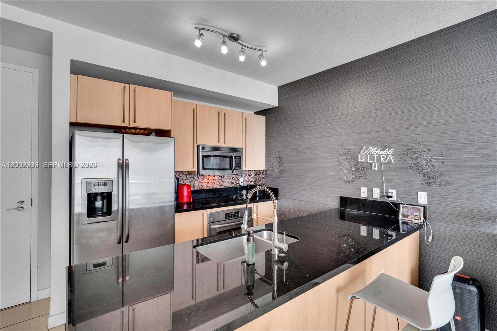 A modern kitchen features light wood cabinets, black granite countertops, and a stainless steel refrigerator — 79 SW 12th St # 1605, Miami FL 33130, MIAMI, FL