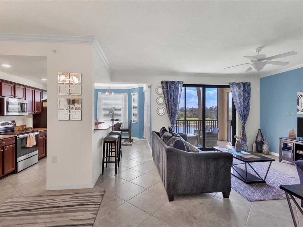 An open-concept living room and kitchen with tile floors, a gray sofa, and balcony views — 16804 VARDON TERRACE UNIT 306, BRADENTON, FL