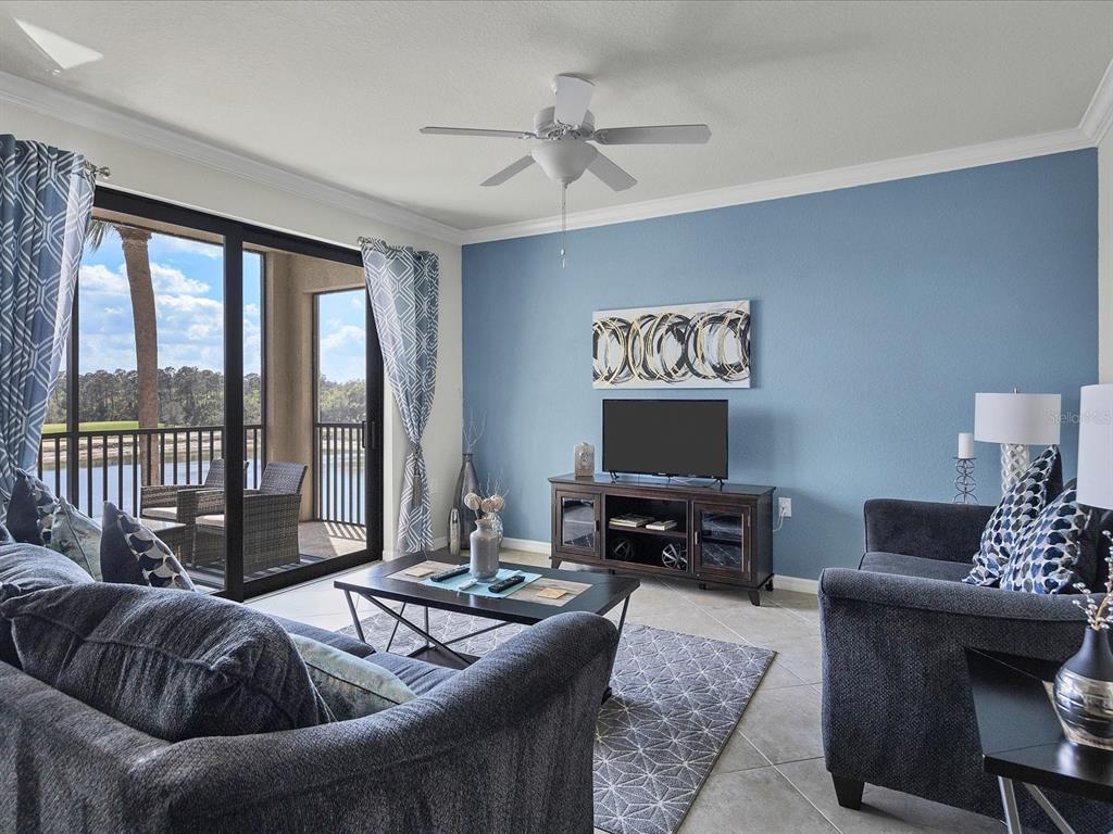 A living room features a blue accent wall, dark furniture, and a balcony overlooking water — 16804 VARDON TERRACE UNIT 306, BRADENTON, FL