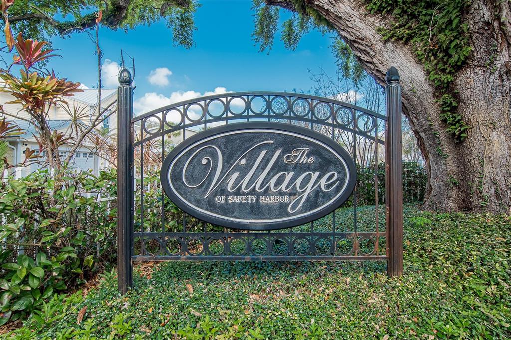 A black metal sign for The Village of Safety Harbor stands in a garden — 918 WOODBRIDGE COURT, SAFETY HARBOR, FL