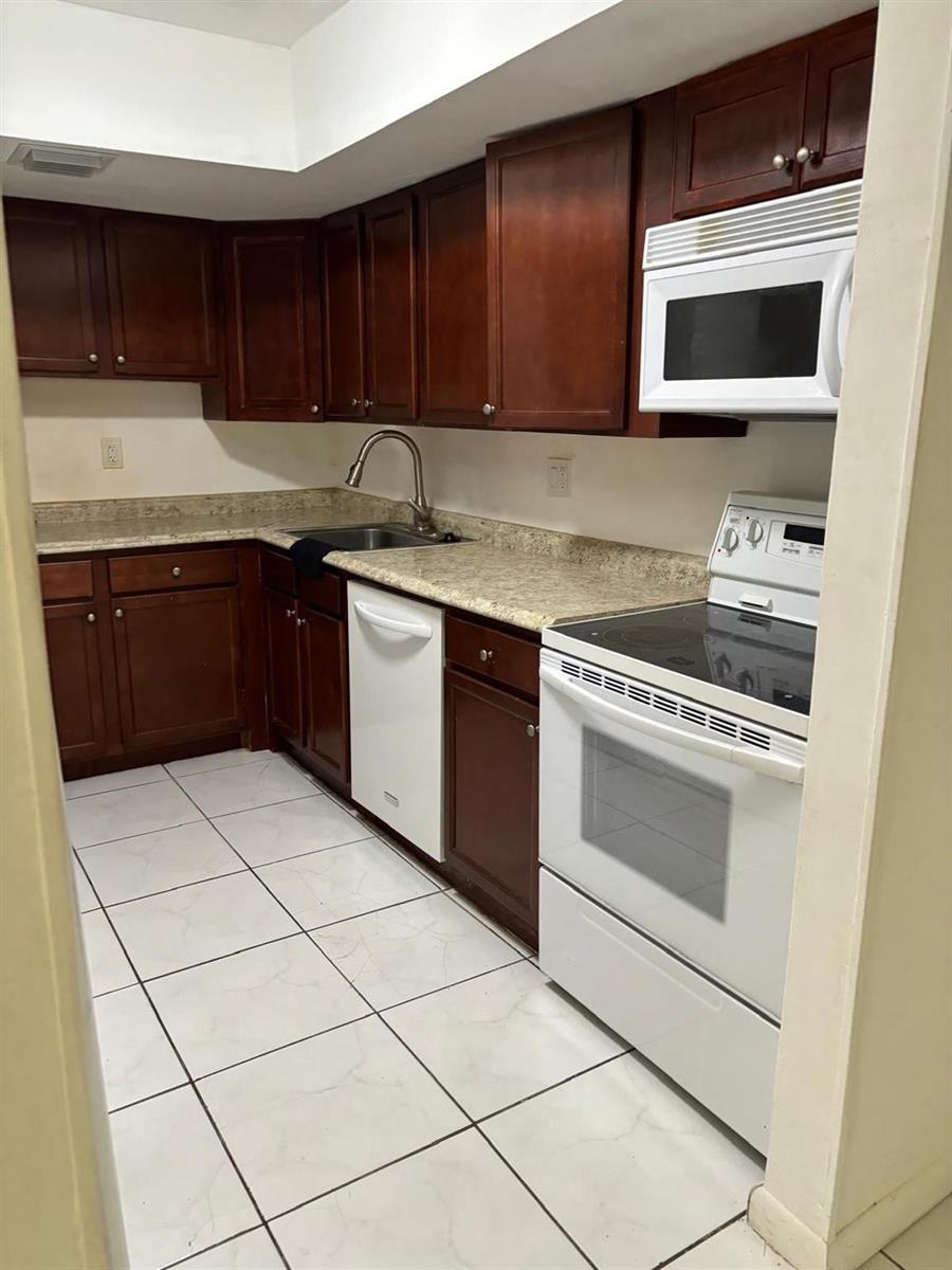 A kitchen features dark wood cabinets, white appliances, a stainless steel sink, and tiled flooring — 2148 NW 57th Avenue # e, Lauderhill FL 33313, LAUDERHILL, FL