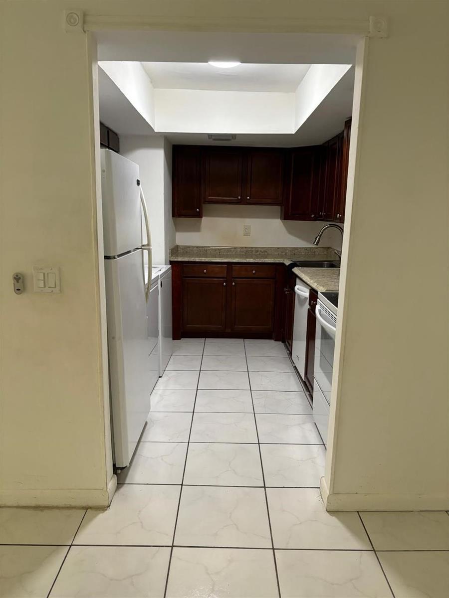 A galley kitchen features dark wood cabinets, granite countertops, white appliances, and white tile flooring — 2148 NW 57th Avenue # e, Lauderhill FL 33313, LAUDERHILL, FL