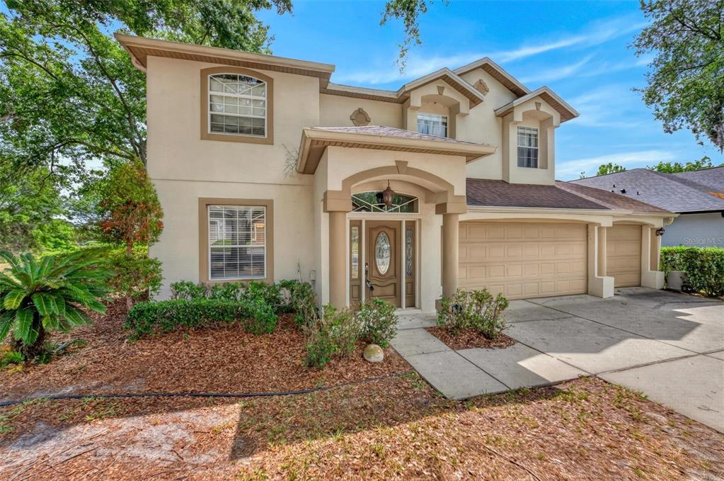 A two-story beige stucco house with a front porch, arched entryway, and three-car garage — 873 PICKFAIR TERRACE, LAKE MARY, FL