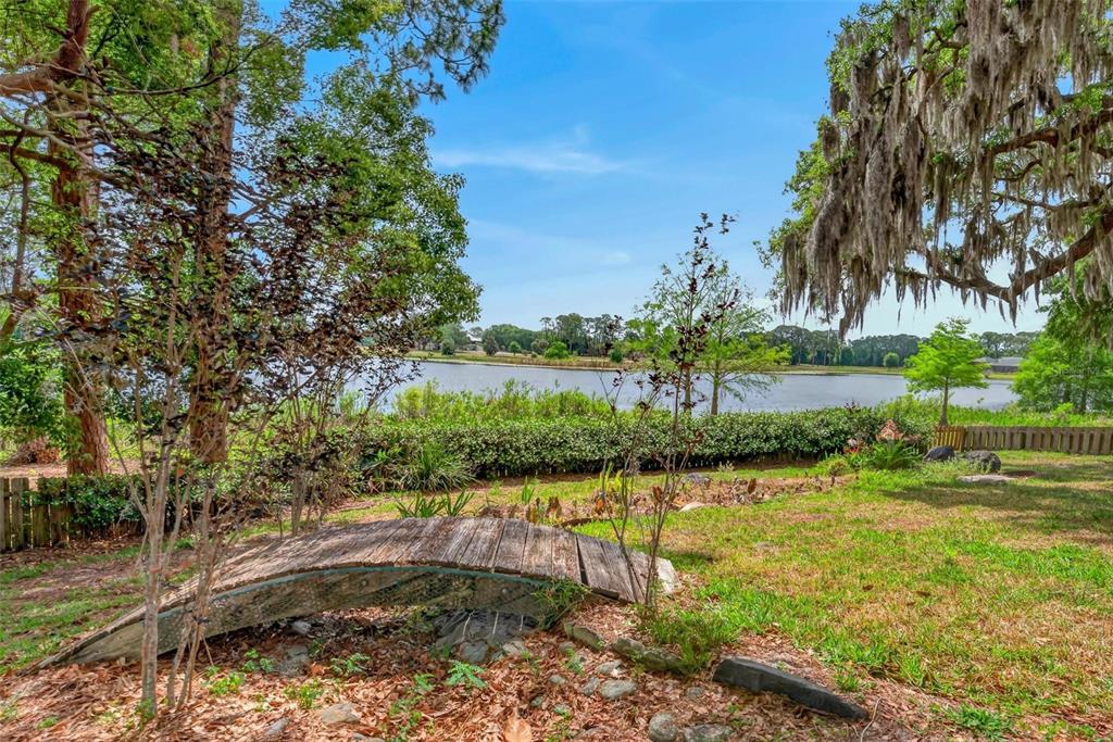 A wooden footbridge sits in a grassy backyard overlooking a lake surrounded by trees — 873 PICKFAIR TERRACE, LAKE MARY, FL