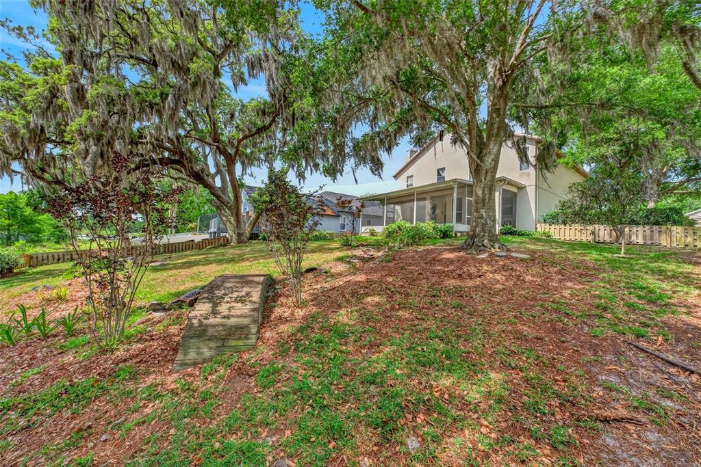 A backyard with a small wooden bridge, mature trees with Spanish moss, and a house — 873 PICKFAIR TERRACE, LAKE MARY, FL